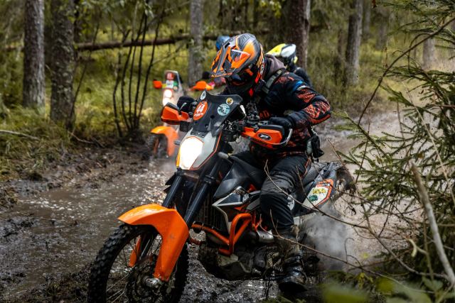 Oranzi tsikliga sõitja pritsib pori metsarajal