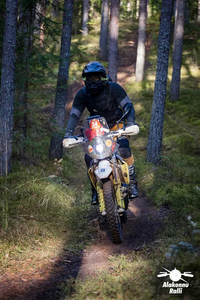 Alakonnu Ralli 2026: tumedas varustuses sõitja sõidab tuledega mootorrattal läbi metsa.