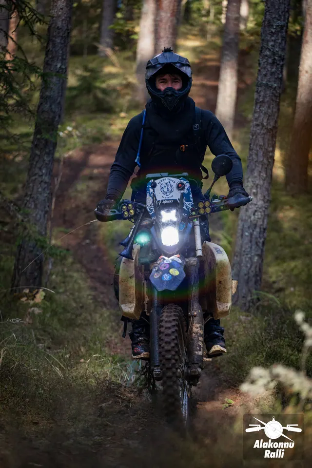 Alakonnu Ralli 2026: musta riietusega sõitja läheneb põleva esitulega mootorrattal.