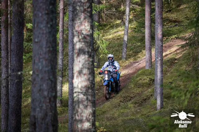 Alakonnu Ralli 2026: sinisel mootorrattal sõitja läheneb eemalt kõrgete puude vahel.