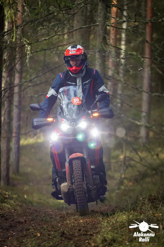 Alakonnu Ralli 2026: punase kiivriga sõitja kõrge tuuleklaasiga rattal varjulises metsas.