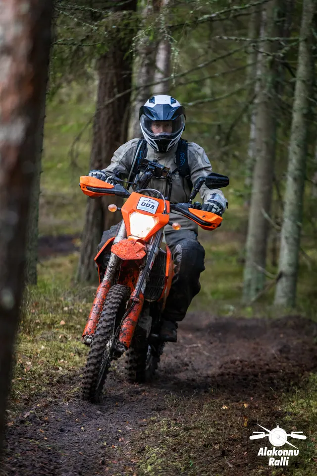 Alakonnu Ralli 2026: valge kiivriga sõitja oranžil enduromootorrattal metsakurvis.