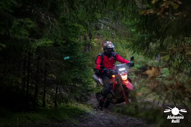 Alakonnu Ralli 2026: punase jakiga mootorrattur läbib varjulist kurvi kuuskede vahel.