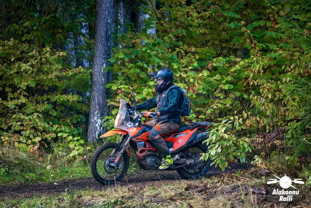 Alakonnu Ralli 2026: seljakotiga sõitja oranžil matkaenduromootorrattal sügisese võsa ees.