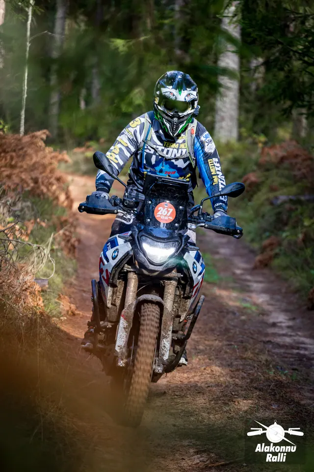 Alakonnu Ralli 2026: sinise ja valge varustusega mootorrattur päikeselaigulisel metsateel.