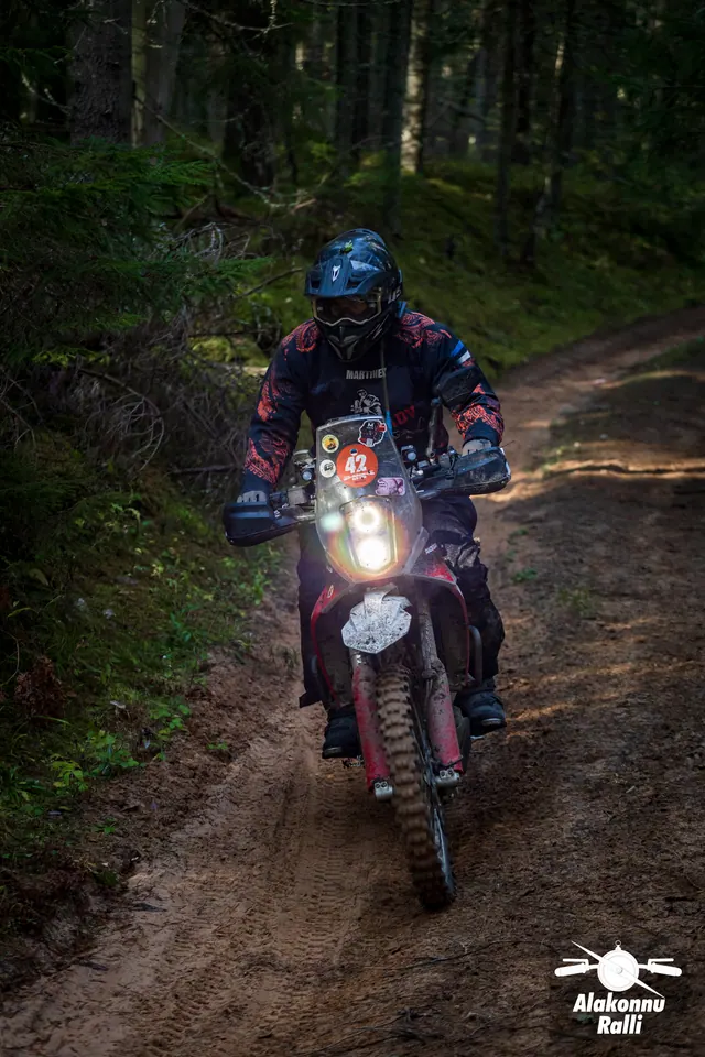 Alakonnu Ralli 2026: mootorrattur punase esiporilauaga rattal läheneb mööda metsateed.