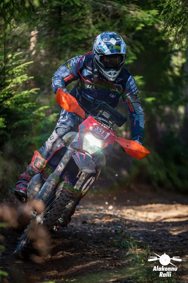 Alakonnu Ralli 2026: mootorrattur oranžide käekaitsmetega rattal kallutab metsakurvis.