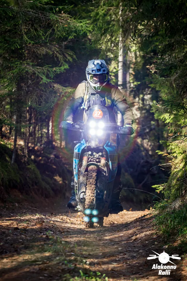 Alakonnu Ralli 2026: mootorrattur ereda esitulega rattal läheneb päikeselisel metsarajal.