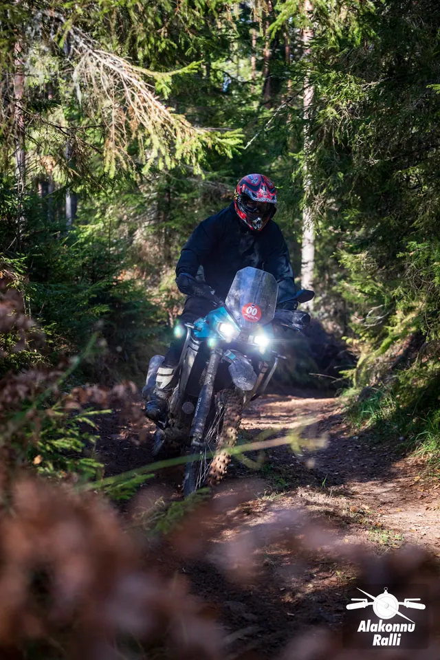 Alakonnu Ralli 2026: punase kiivriga sõitja läheneb kõrge tuuleklaasiga rattal metsakurvis.