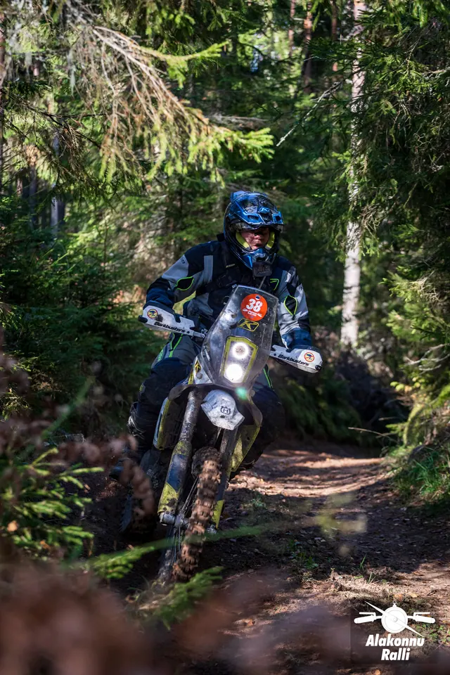 Alakonnu Rally 2026: a rider in a blue helmet on a yellow and blue motorcycle at a forest bend.