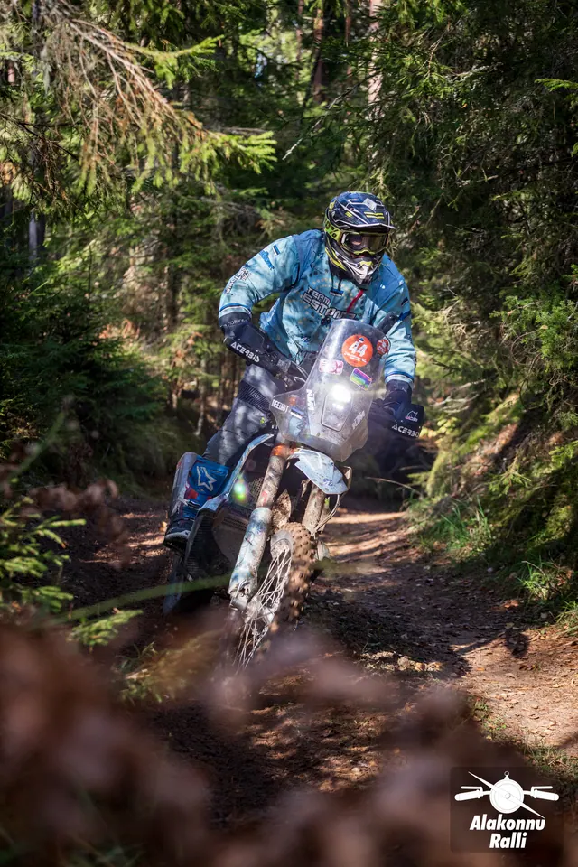 Alakonnu Rally 2026: a rider in light blue gear leans the bike between spruce trees.