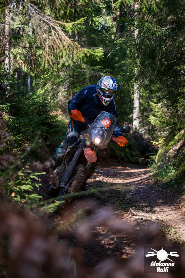 Alakonnu Rally 2026: a rider on a bike with orange handguards leans deeply into a forest bend.