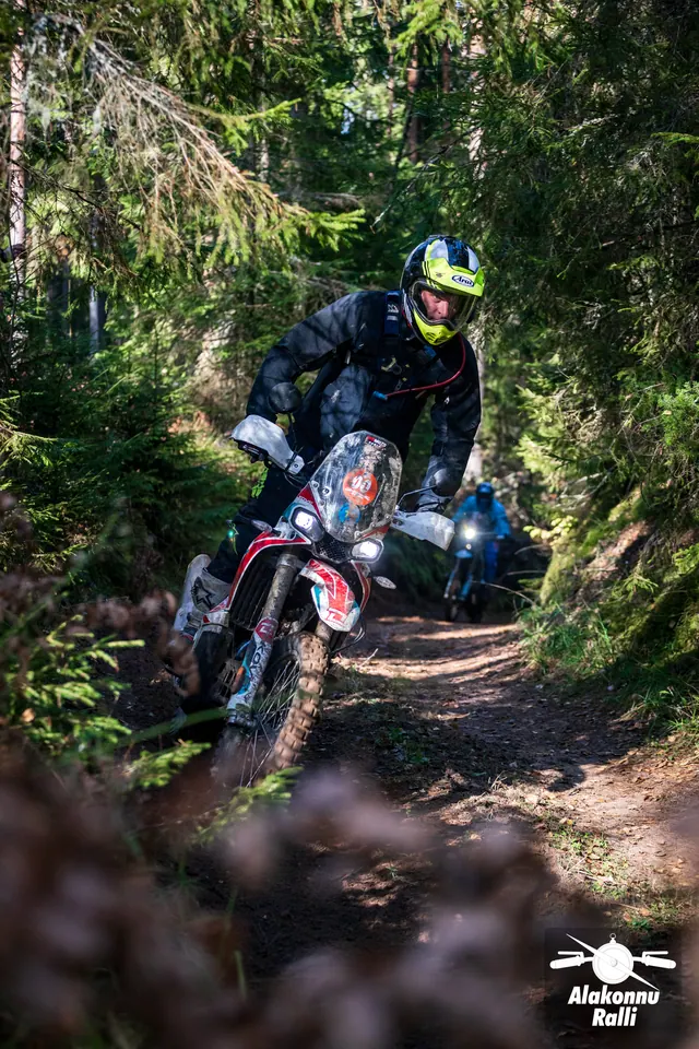 Alakonnu Rally 2026: a rider in a yellow helmet on a red bike leans into a forest bend.