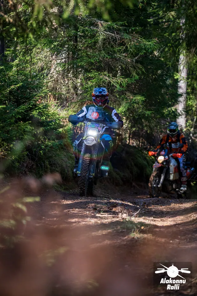 Alakonnu Rally 2026: two riders approach along a shaded spruce forest trail.