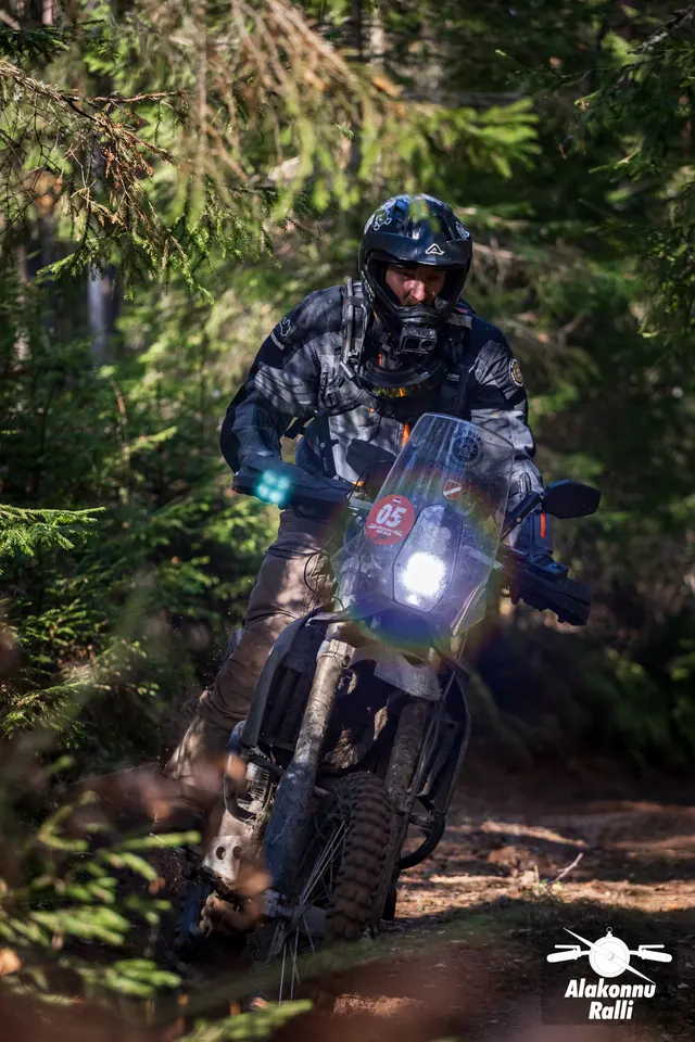 Alakonnu Rally 2026: a rider in black gear on a muddy adventure motorcycle at a forest bend.