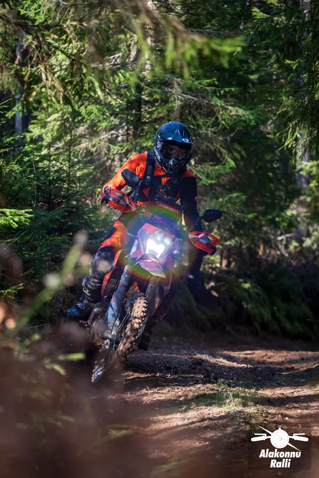 Alakonnu Rally 2026: a rider in red and blue gear leans a red motorcycle in the woods.