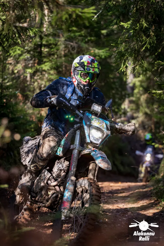 Alakonnu Rally 2026: a motorcyclist on a light-coloured enduro bike in a bend with another rider farther back.