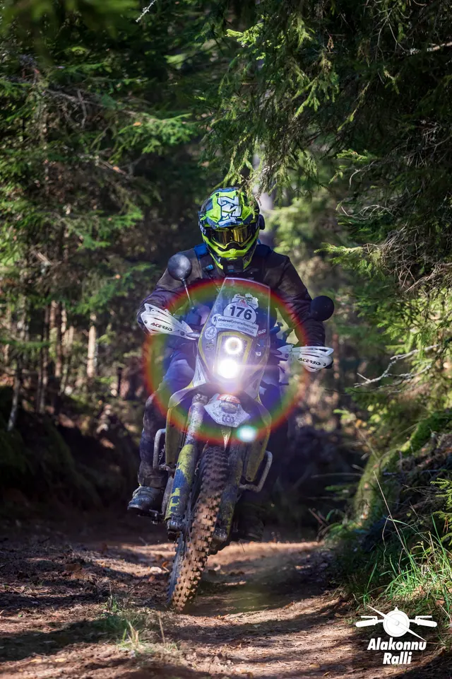 Alakonnu Rally 2026: a rider in a bright helmet approaches with the headlight on along a forest trail.