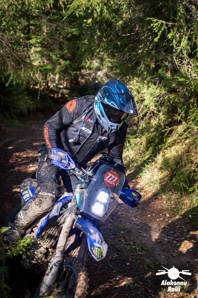 Alakonnu Rally 2026: a rider on a blue motorcycle leans deeply into a forest trail bend.