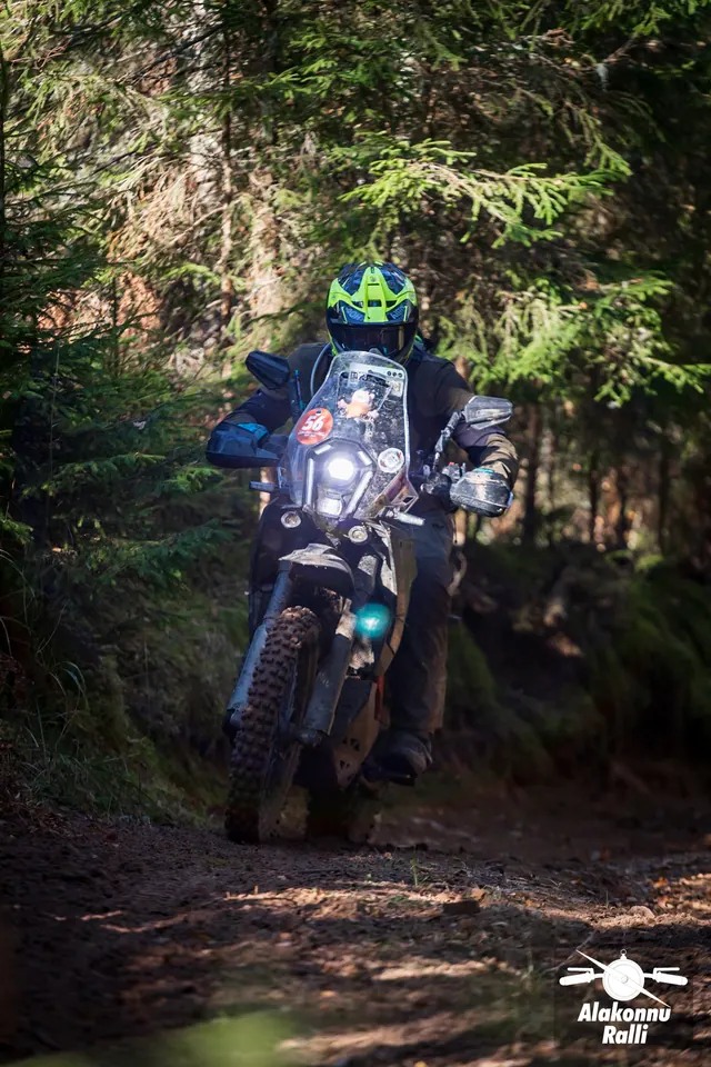 Alakonnu Rally 2026: a rider in a yellow helmet on a dark bike with a tall windscreen in the woods.