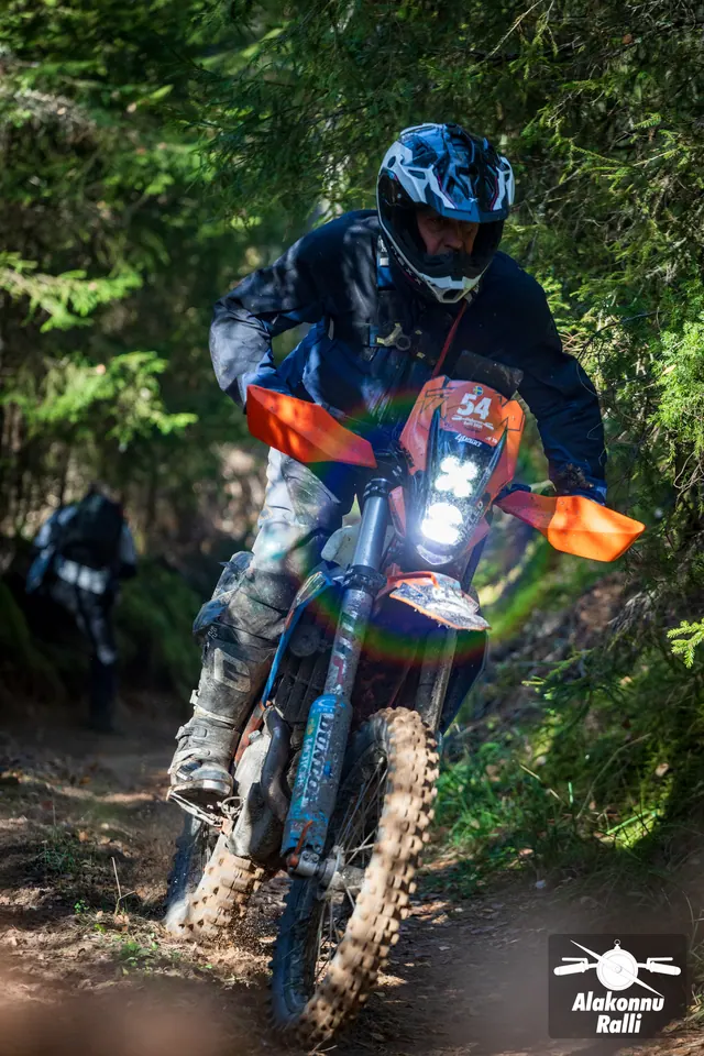 Alakonnu Ralli 2026: oranžide käekaitsmetega rattal sõitja seisab jalaraudadel metsakurvis.