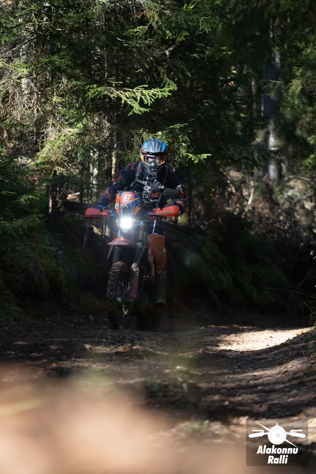 Alakonnu Ralli 2026: mootorrattur läheneb eemalt varjulisel kuuskedega ääristatud rajal.