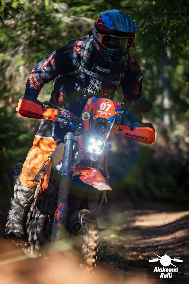 Alakonnu Ralli 2026: oranži ja musta varustusega sõitja oranžil rattal metsakurvis.