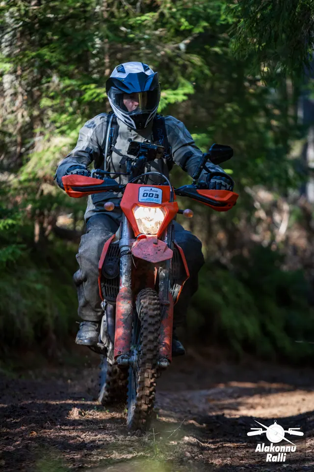 Alakonnu Ralli 2026: halli varustusega sõitja oranžil mootorrattal läheneb metsarajal.