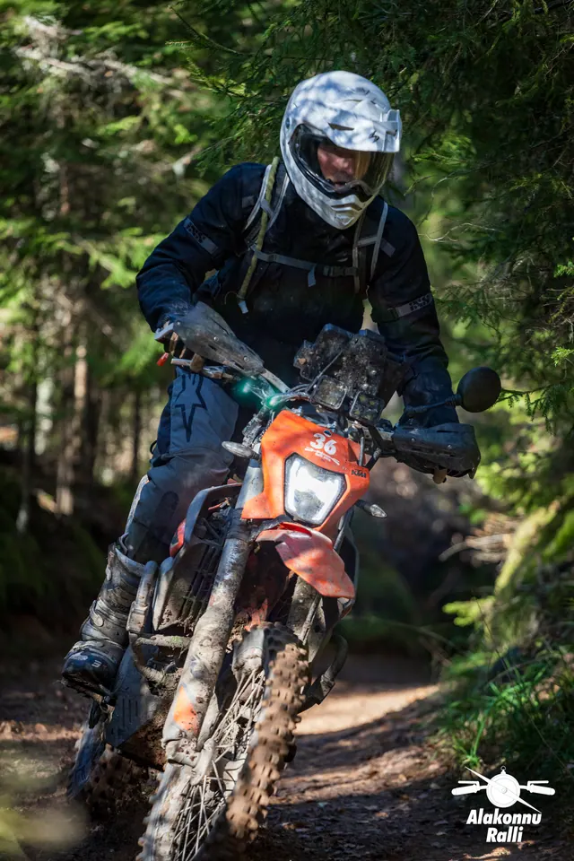Alakonnu Ralli 2026: valge kiivriga sõitja seisab jalaraudadel oranžil enduromootorrattal.