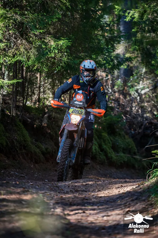 Alakonnu Ralli 2026: mootorrattur oranžide käekaitsmetega rattal läheneb varjulisest metsast.