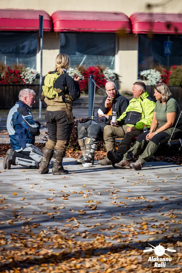 Alakonnu Ralli 2026: inimesed söövad ja puhkavad päikeselisel väljakul hoone ees; osa istub pingil, teised seisavad või põlvitavad kõrval.