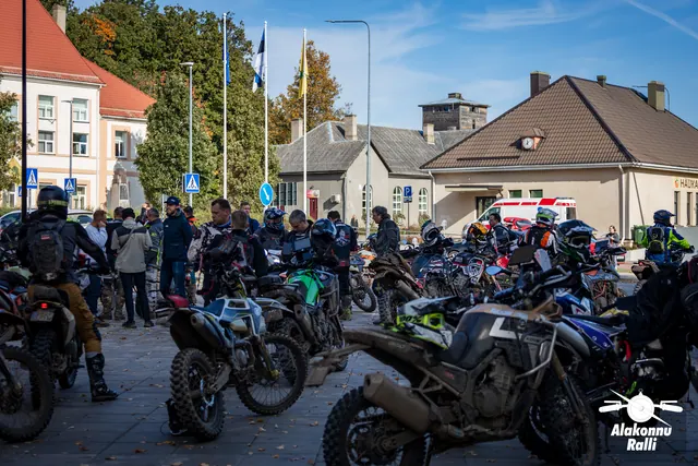 Alakonnu Ralli 2026: mootorratturid ja pargitud rattad hoonetega ümbritsetud väljakul.