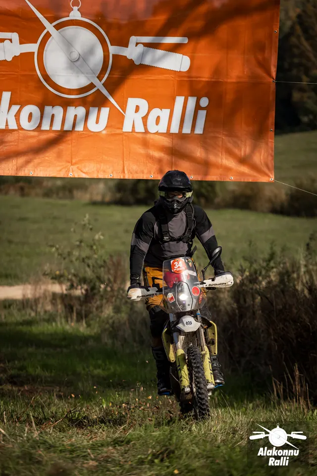 Alakonnu Ralli 2026: mustas varustuses sõitja kollasel mootorrattal oranži rallibänneri all.