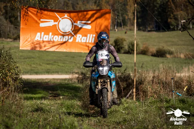 Alakonnu Ralli 2026: halli jakiga sõitja sinisel mootorrattal rohurajal rallibänneri all.