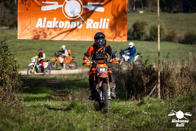 Alakonnu Ralli 2026: oranžis varustuses sõitja oranžil rattal, mootorratturid tagaplaanil.
