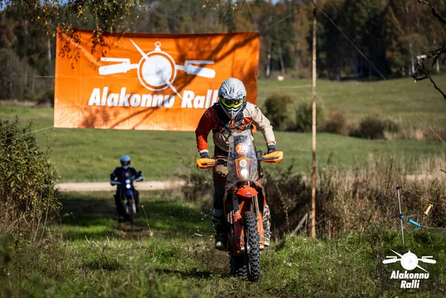 Alakonnu Ralli 2026: halli ja oranži varustusega sõitja oranžil rattal rallibänneri ees.