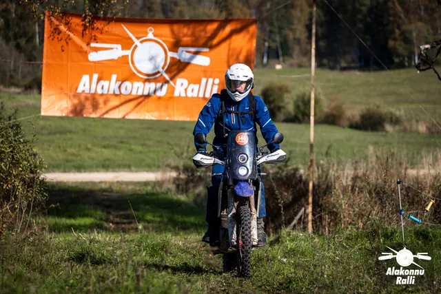Alakonnu Ralli 2026: valge kiivriga sõitja sinisel mootorrattal rohurajal rallibänneri all.