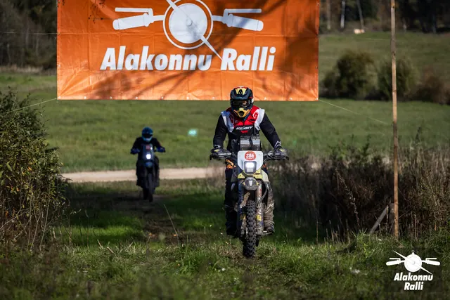 Alakonnu Ralli 2026: värvilise kiivriga sõitja heledal rattal rallibänneri all, teine sõitja taga.