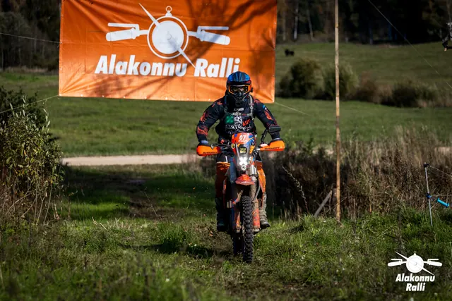 Alakonnu Ralli 2026: oranži ja musta varustusega sõitja oranžil rattal rallibänneri all.