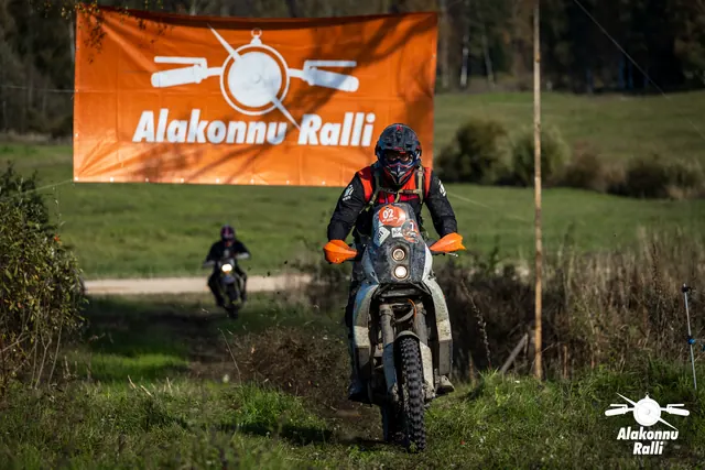 Alakonnu Ralli 2026: punase kiivriga sõitja oranžide käekaitsmetega rattal rallibänneri ees.