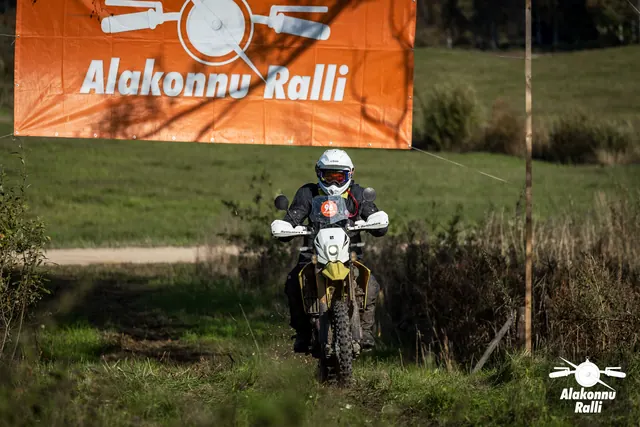 Alakonnu Ralli 2026: valge kiivriga sõitja läheneb kollase esiporilauaga mootorrattal rallibänneri all.