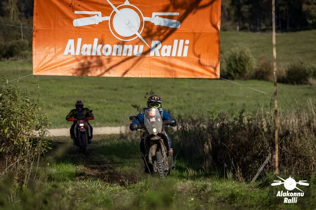 Alakonnu Ralli 2026: kaks mootorratturit sõidavad üksteise järel mööda rohurada oranži rallibänneri all.