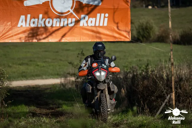 Alakonnu Ralli 2026: tumedas sõiduvarustuses osaleja läheneb oranžide käekaitsmetega mootorrattal.