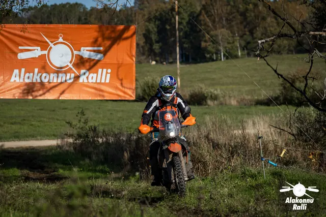Alakonnu Ralli 2026: sinise ja valge kiivriga sõitja läheneb oranžil mootorrattal rohuraja ääres kasvavate põõsaste vahel.