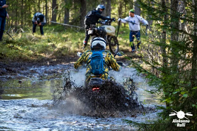 Alakonnu Ralli 2026: sinise seljakotiga sõitja läbib metsaraja veetakistust, teised ootavad vastaskaldal.