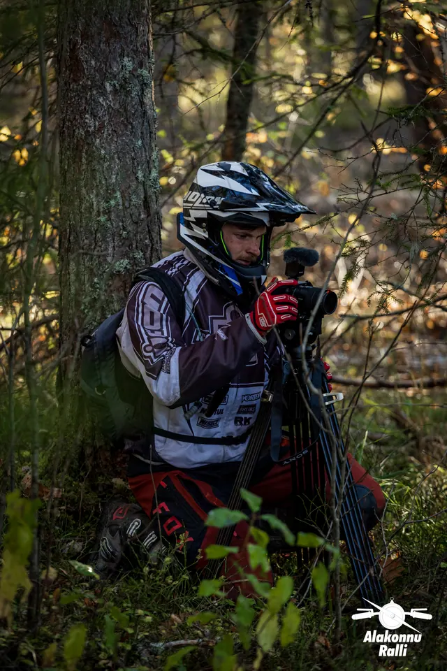 Alakonnu Rally 2026: a helmeted person in riding gear handles a camera on a tripod in the forest.
