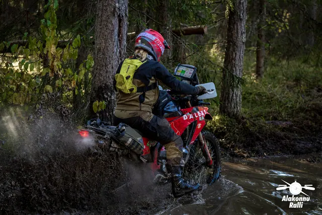 Alakonnu Rally 2026: a rider in a red helmet with a yellow backpack throws up muddy water on a red motorcycle.