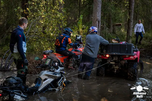 Alakonnu Rally 2026: people stand beside motorcycles and an ATV in the flooded track, with a tow rope attached to the ATV.