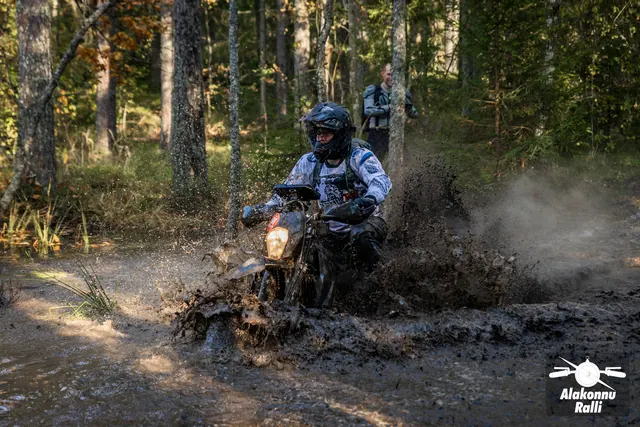 Alakonnu Rally 2026: a motorcyclist rides through a flooded forest track with a muddy spray rising behind the rear wheel.