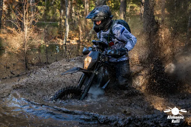 Alakonnu Rally 2026: a rider leans the motorcycle in a flooded forest track as muddy water sprays to the side.